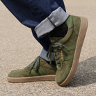 model standing outdoors in mens larch barefoto trainer in green worn with blue jeans