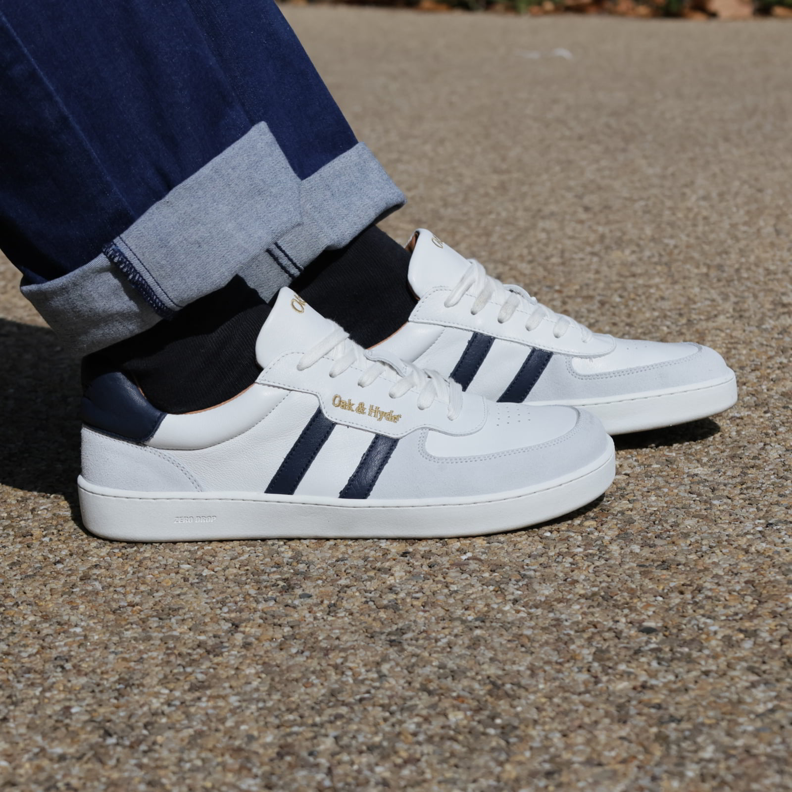 model wearing mens larch barefoot trainers in white navy with dark blue jeans