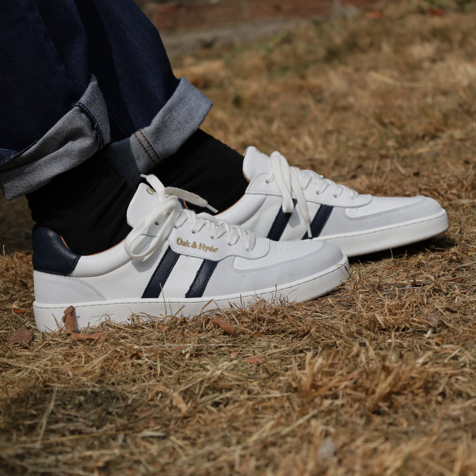 model wearing mens larch barefoot trainers in white navy with dark blue jeans