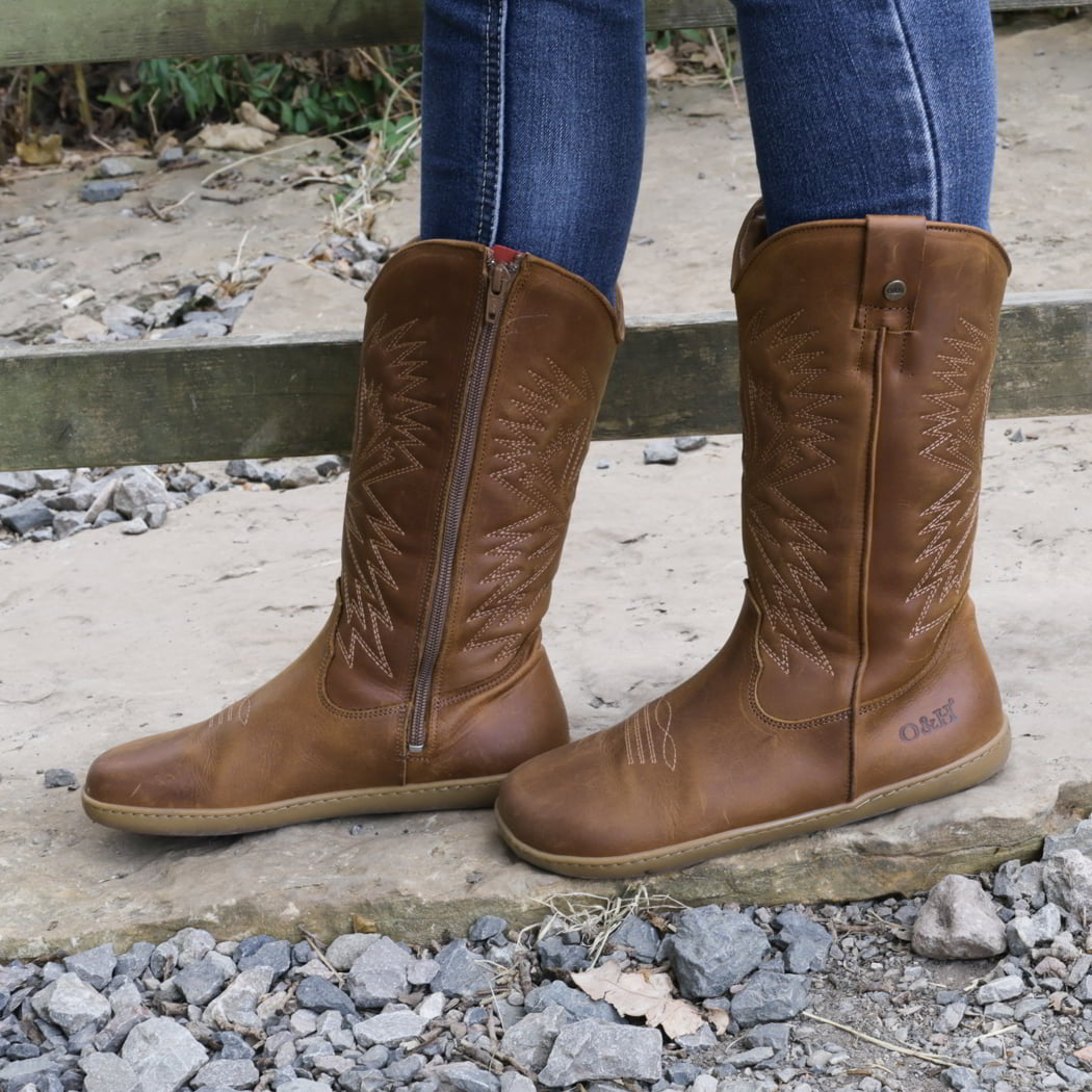 model standing outdoors by a gate wearing mesquite barefoot cowboy boots in cognac