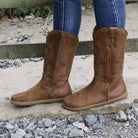 model standing outdoors by a gate wearing mesquite barefoot cowboy boots in cognac