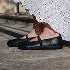 person wearing black olive barefoot mary jane shoes with a white dress sitting outside 