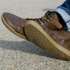 person wearing redwood dark brown barefoot boots with jeans sitting on bench