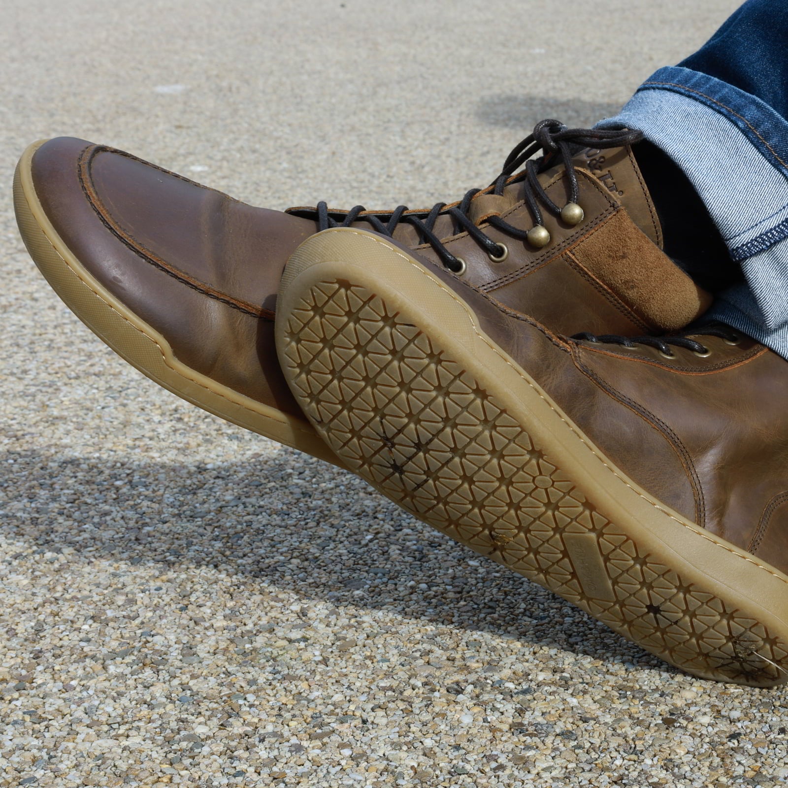 person wearing redwood dark brown barefoot boots with jeans sitting on bench