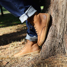 model wearing redwood barefoot boots with blue jeans rolled up leaning against a tree