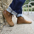 model standing outdoors wearing spruce barefoot ankle boots in tan with blue jeans