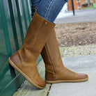 model wearing mid calf tan barefoot boots with blue jeans on concrete floor