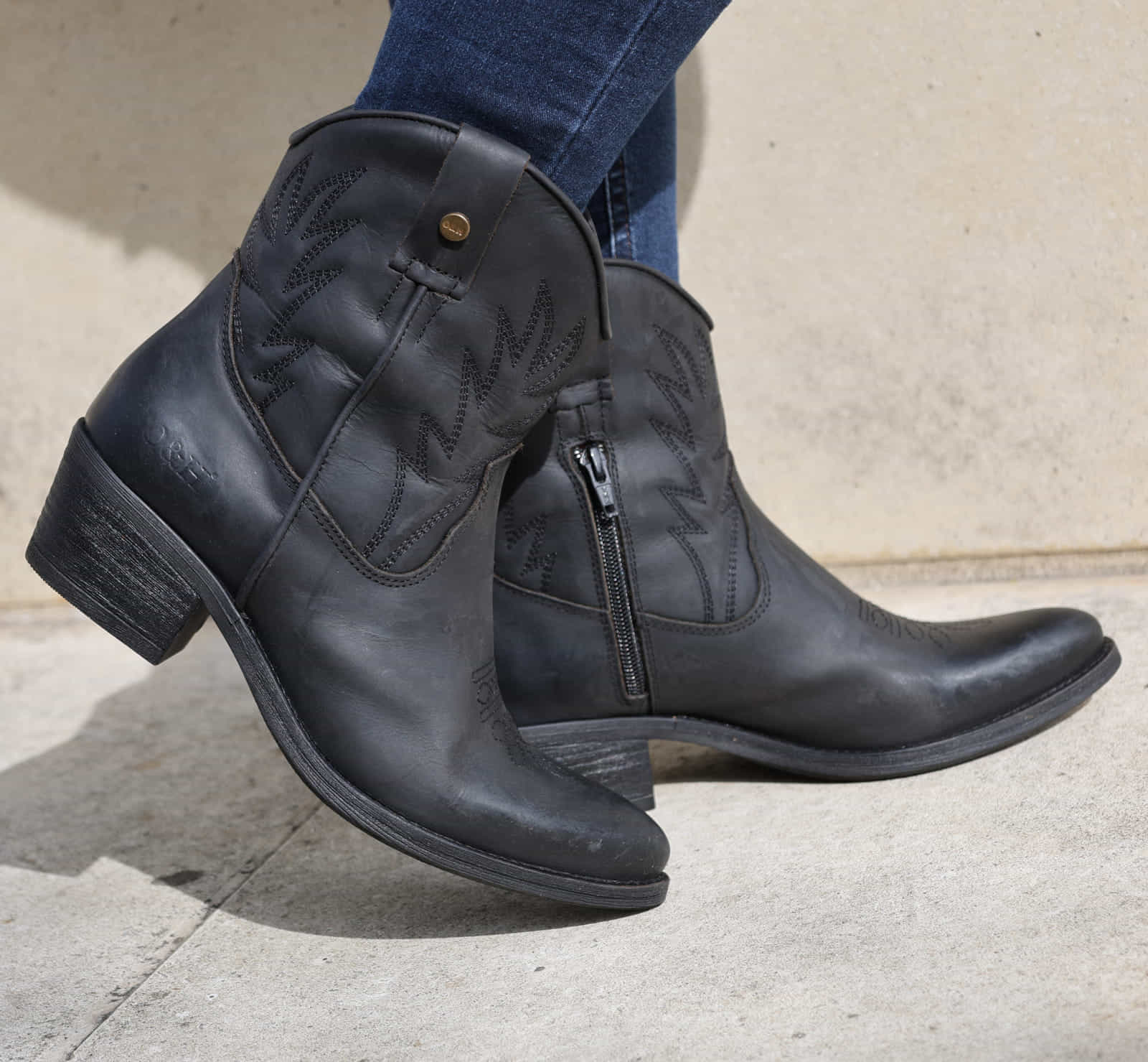 model wearing black cowboy boots with blue jeans on concrete