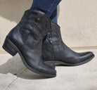 model wearing black cowboy boots with blue jeans on concrete