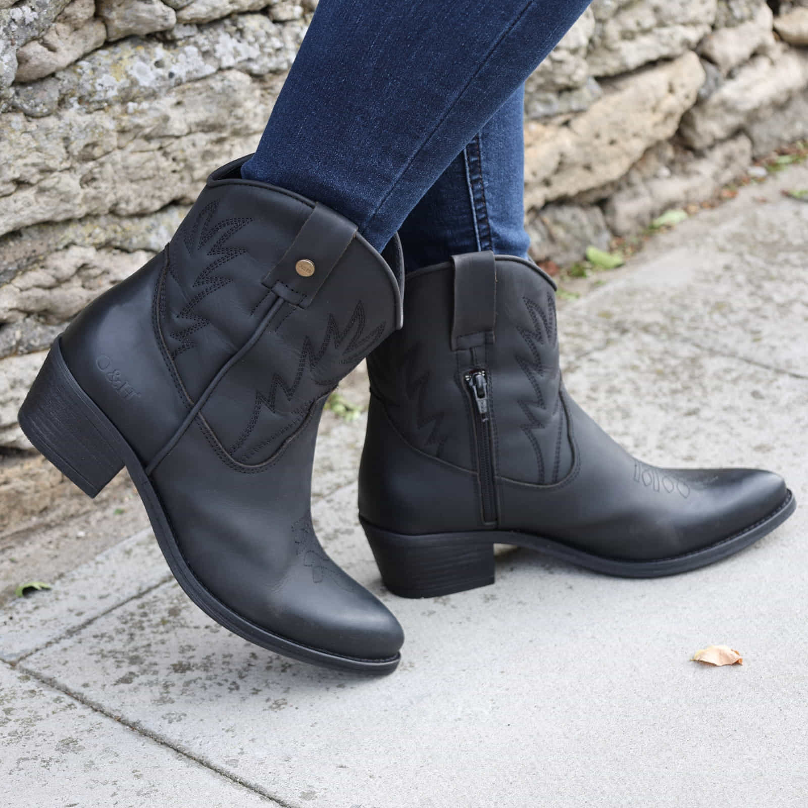 persons legs showing black ankle boots worn with jeans on pavement