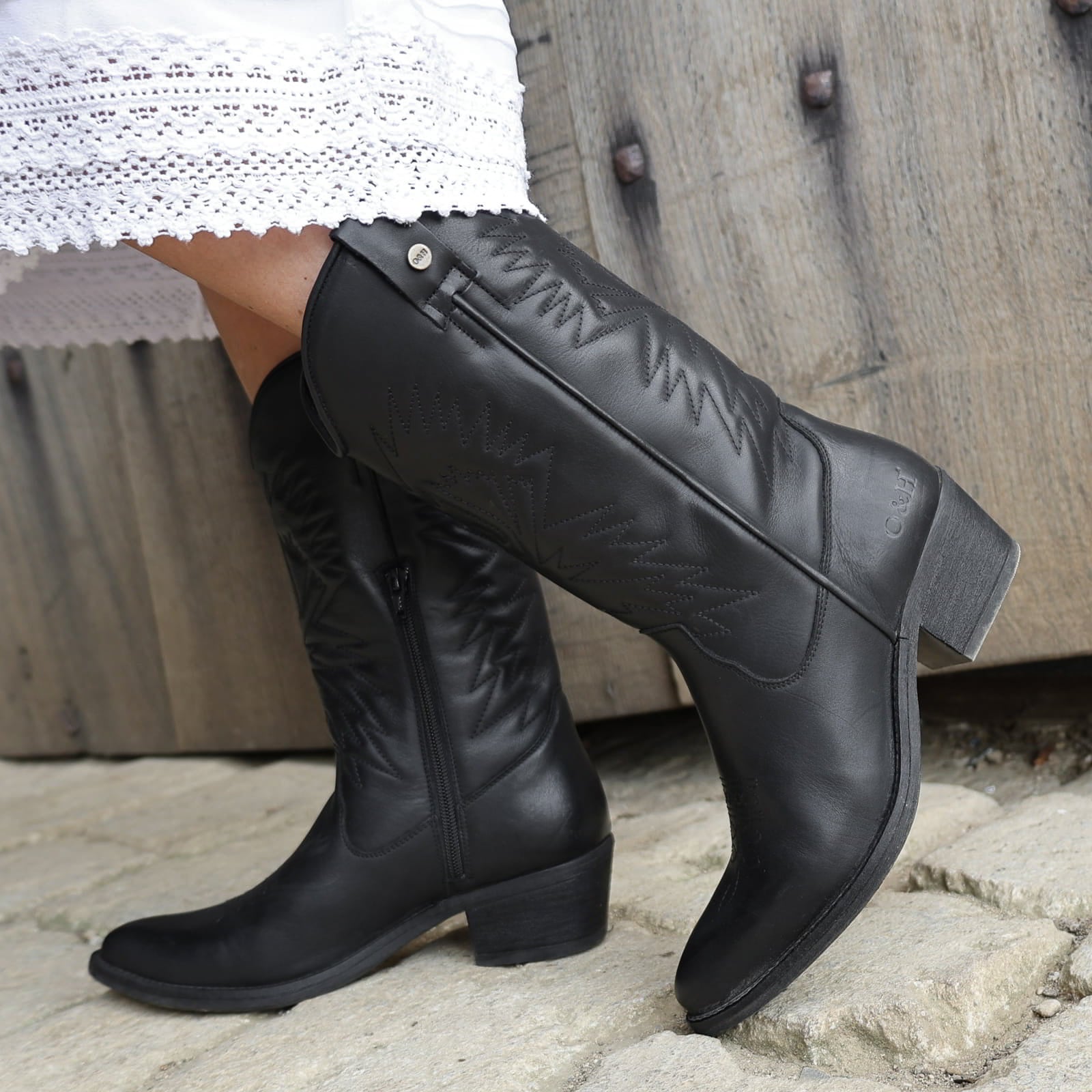 model wearing black leather texan hi cowboy boots with a white dress on a stone floor