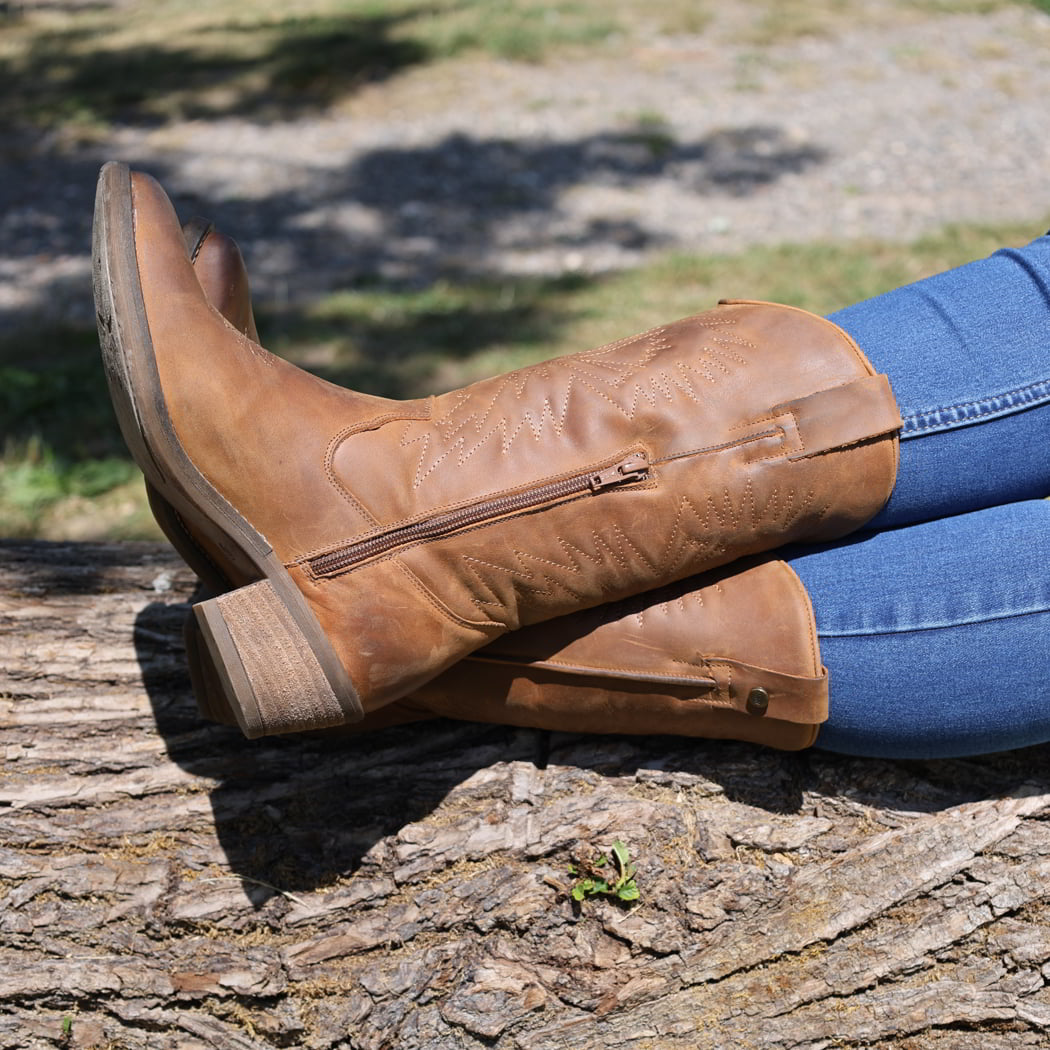 person wearing texan Hi cowboy boots in cognac sitting on a log outside