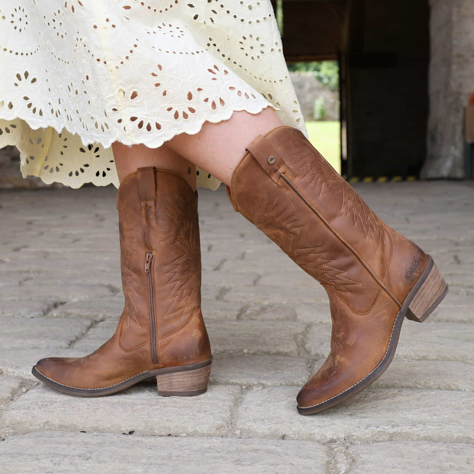 Brown knee-high boots worn with a yellow lace dress on a stone pavement.