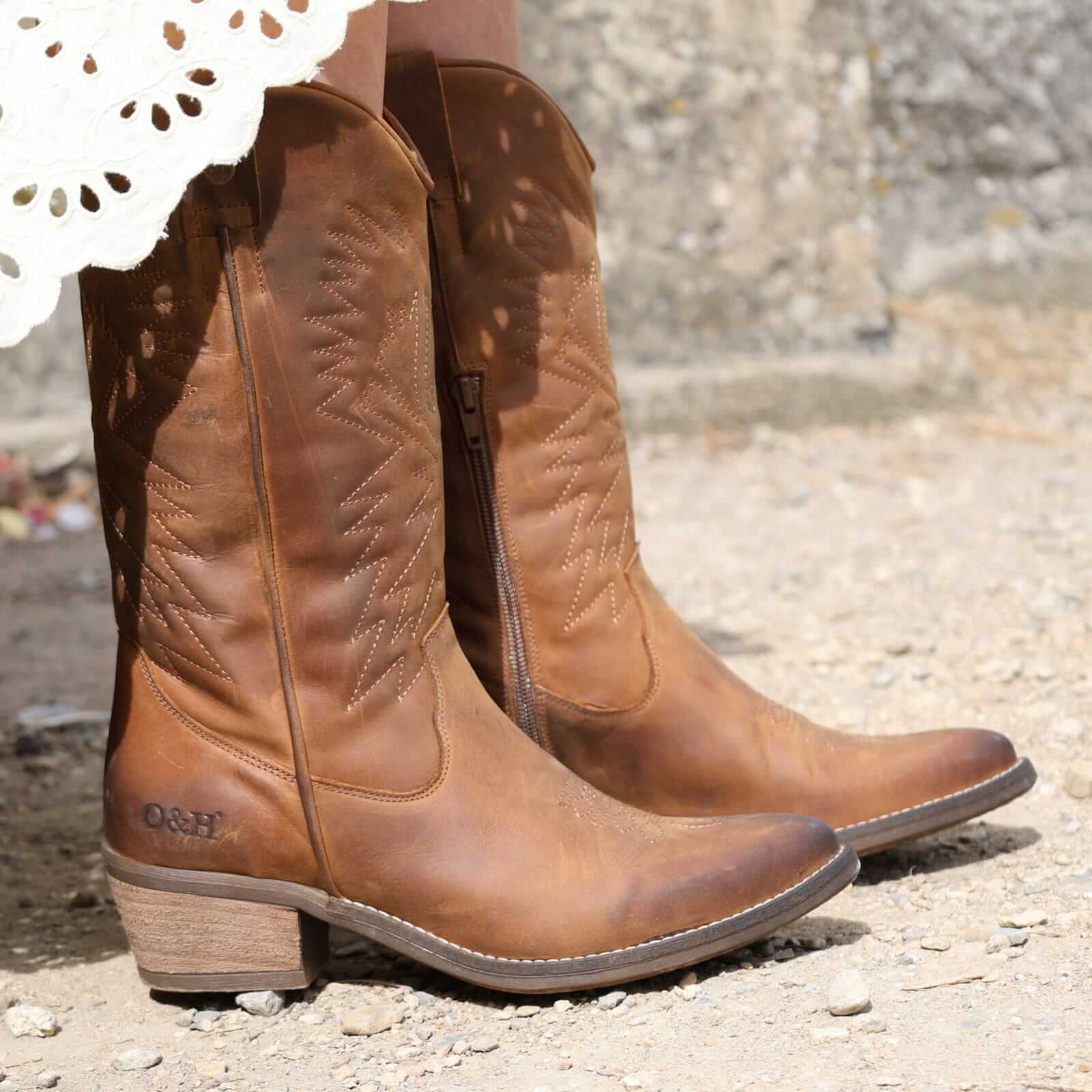 Brown leather cowboy boots on a textured ground surface