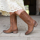 Brown knee-high boots worn with a white lace dress on a stone pavement.