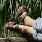 model wearing wisteria barefoot sandals in brown sitting outdoors showing top down view