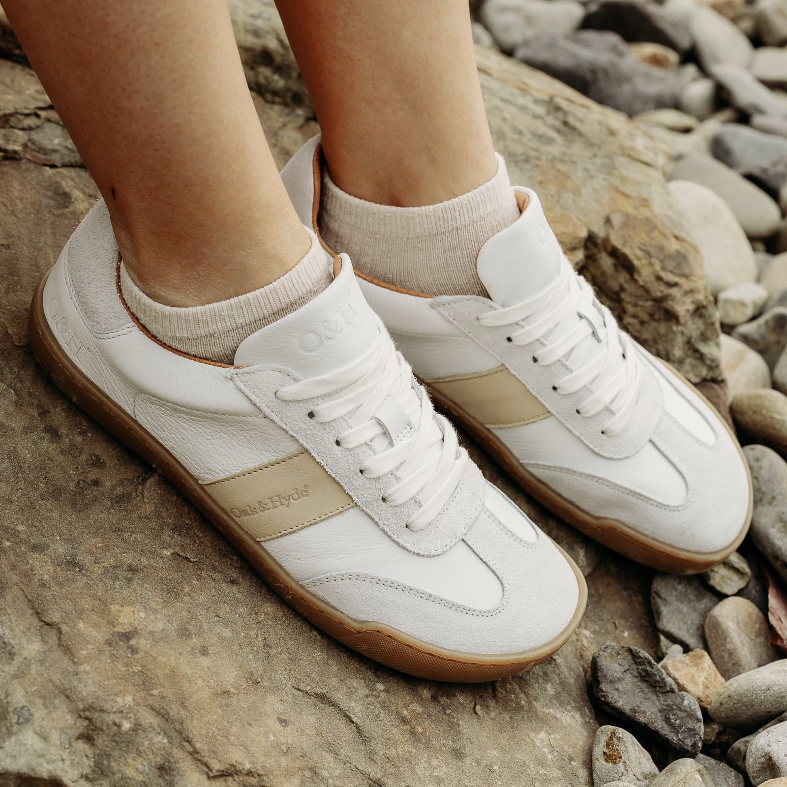 model sitting on rock wearing juniper white beige barefoot trainers