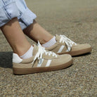 person wearing womens larch barefoot trainers in beige sitting on a bench outdoors