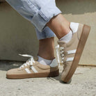 model standing outdoors wearing womens larch barefoot trainers in beige with blue jeans