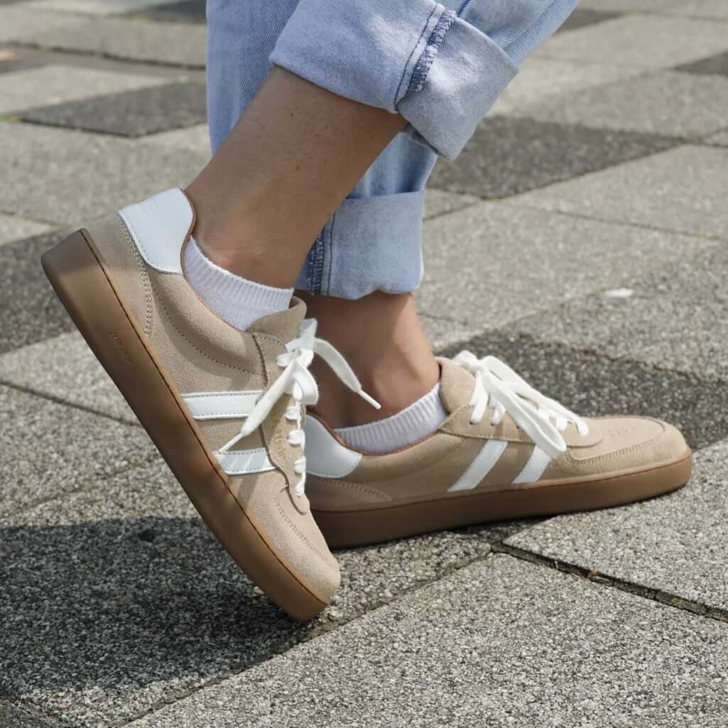 model standing on a pavement wearing larch barefoot trainers in beige with blue jeans