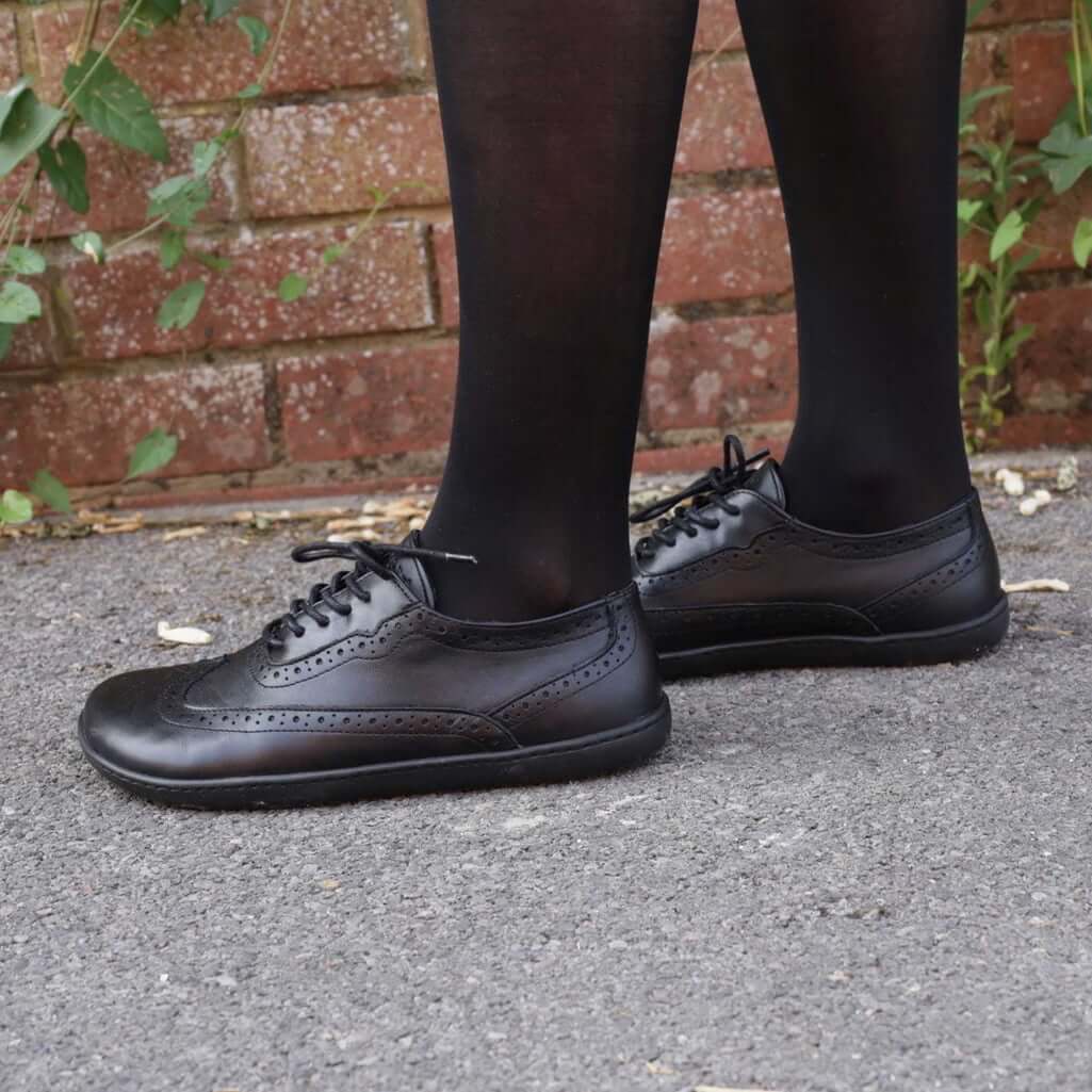 model standing on pavement in black maple brogue barefoot shoes worn with black tights