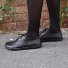 model standing on pavement in black maple brogue barefoot shoes worn with black tights