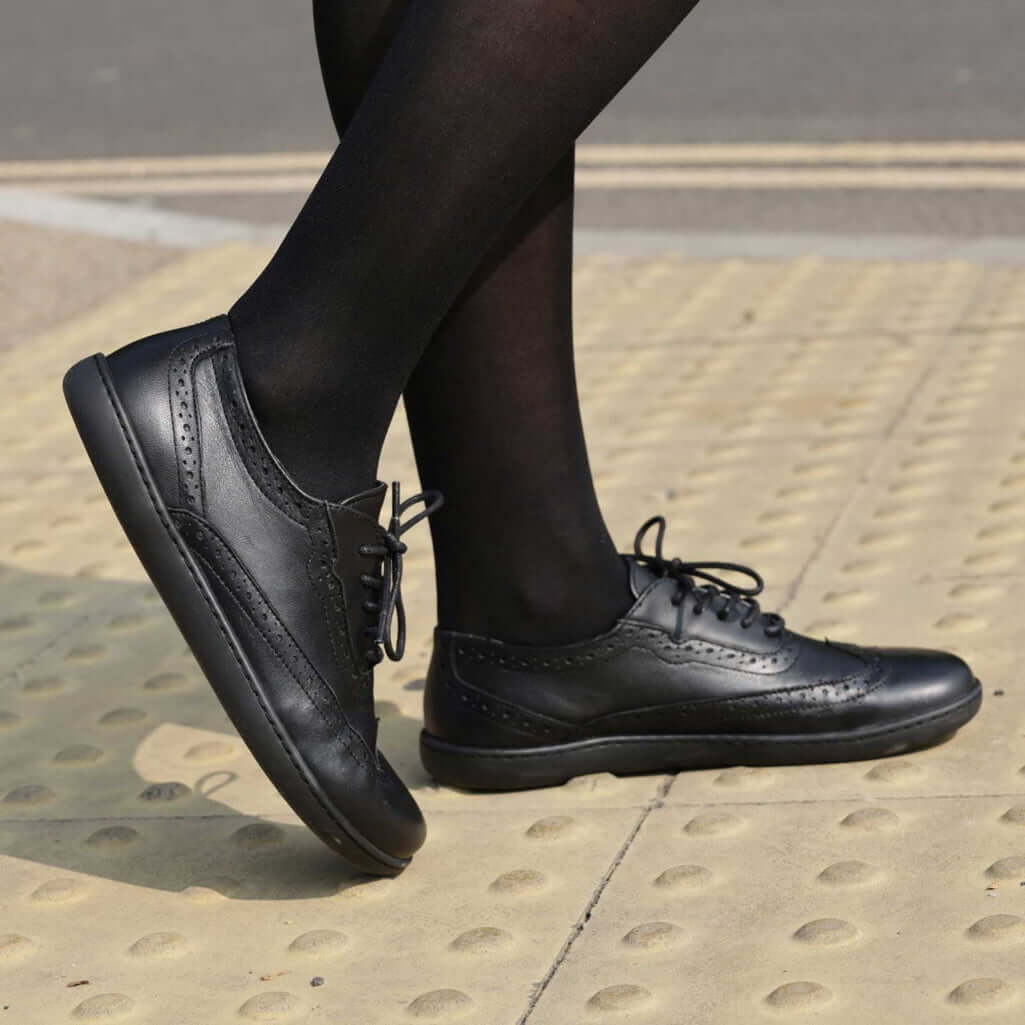 model wearing womens maple brogue barefoot shoes in black standing on pavement