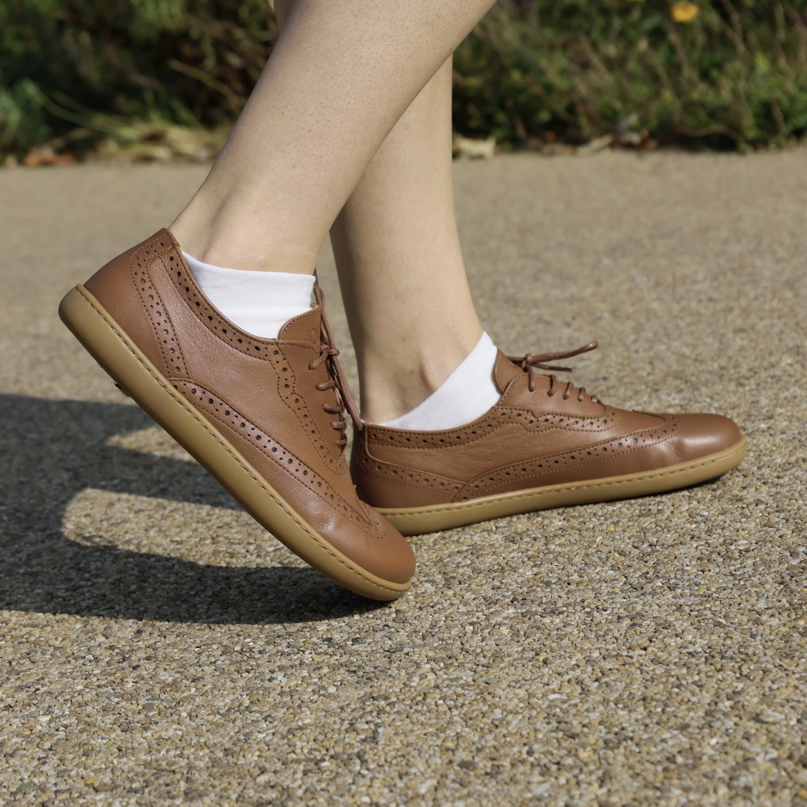 model standing outdoors wearing maple brogue barefoot shoes in tan